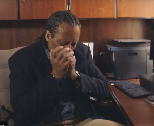 Dr. Harris sitting at his desk playing blues harmonica.