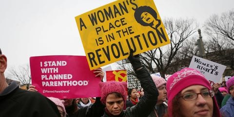 Women holding protest signs that say 'a woman's place is in the revolution'